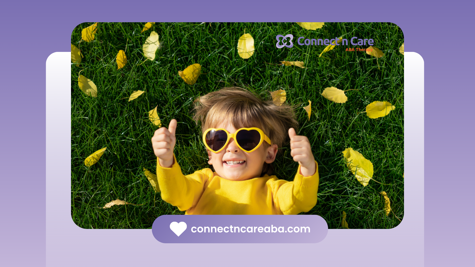 A little boy wearing sunglasses is laying in the grass and giving a thumbs up.