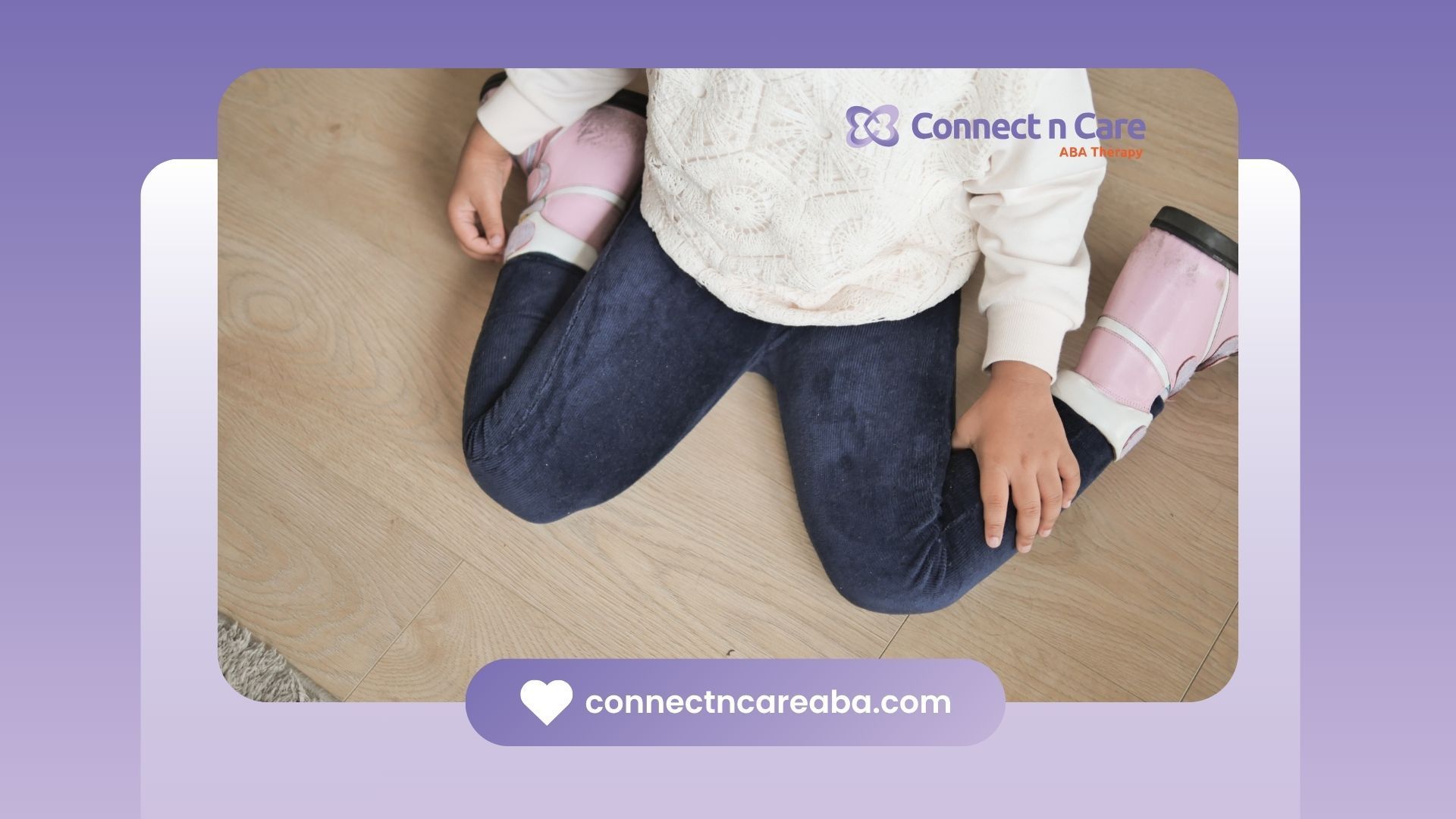 Child kneeling on wooden floor, wearing jeans, sweater, and pink leg braces.