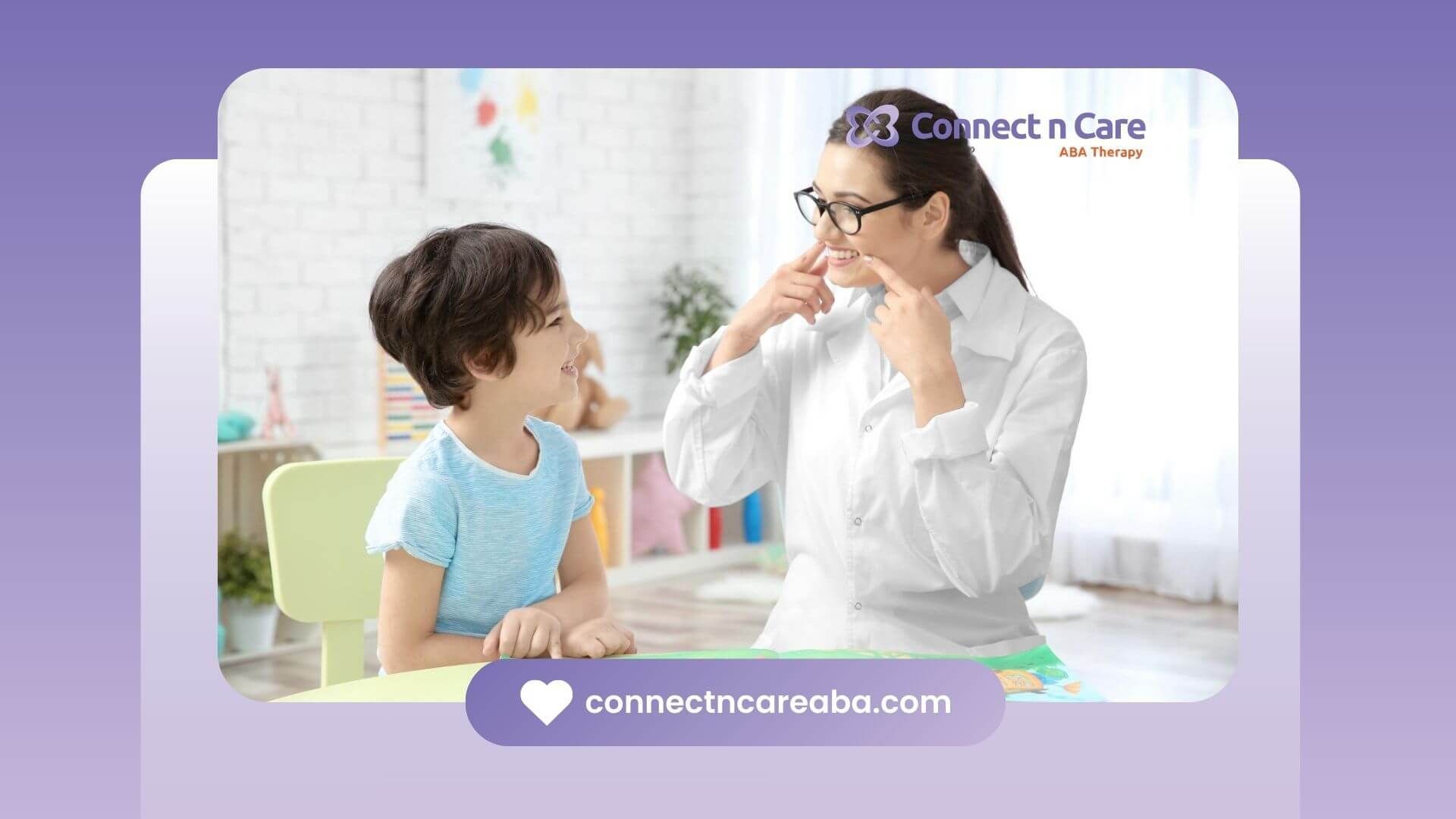 A BCBA smiles and points to her mouth while reading with a child in ABA therapy.