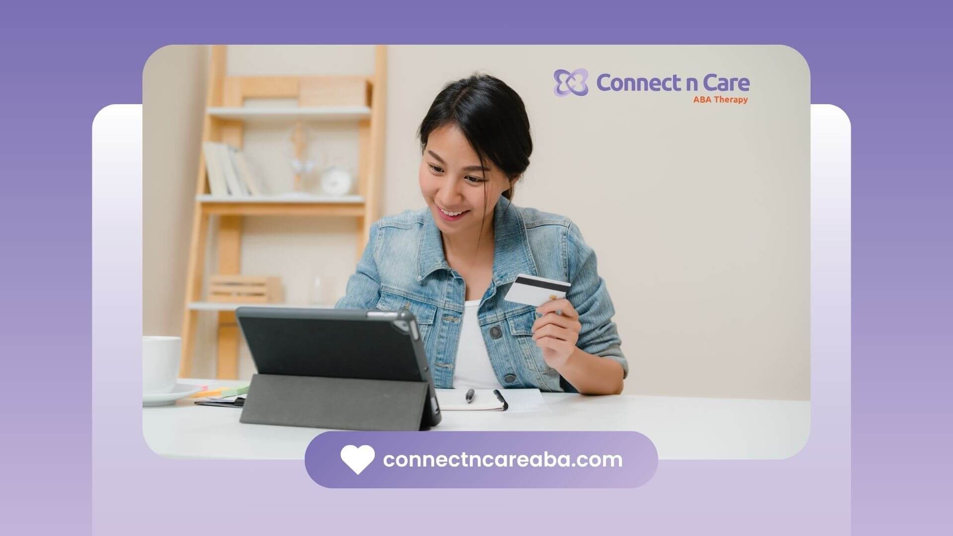 The female ABA therapist smiling while shopping online, holding a credit card and a tablet.