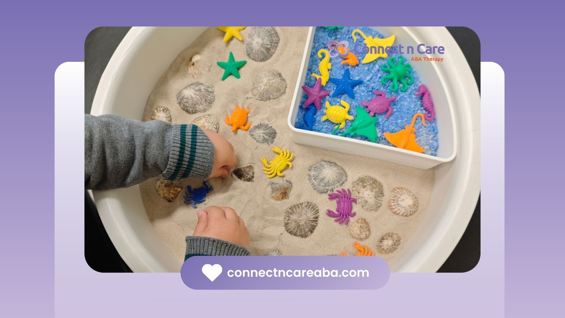 Child's hands playing with sand and sea animal toys in a white bin.