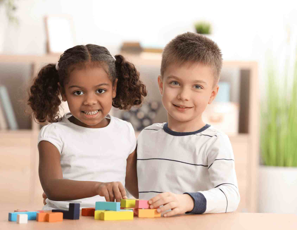 A boy and a girl sitting at a table playing with wooden blocks 