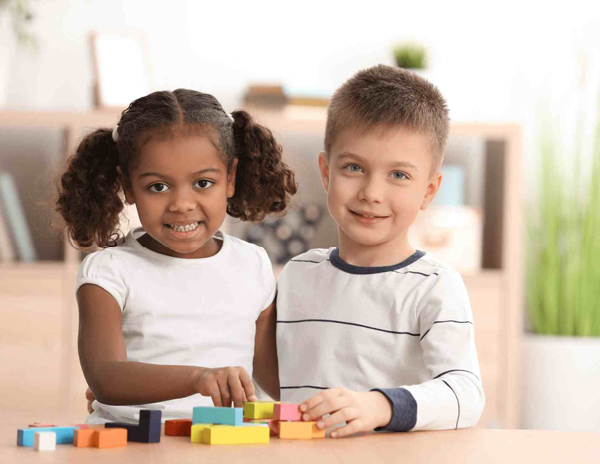 A boy and a girl sitting at a table playing with wooden blocks