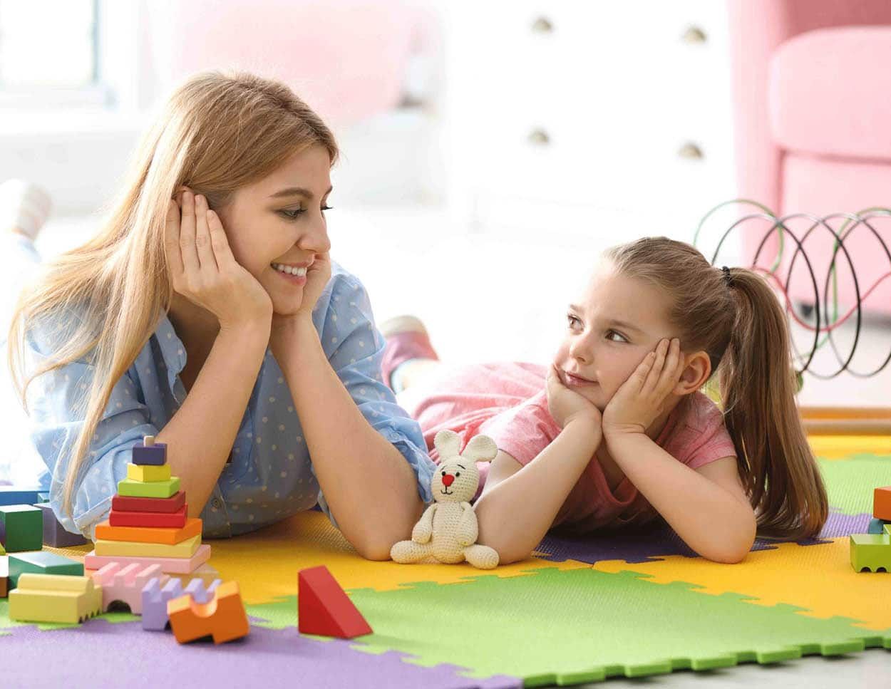 A woman and a little girl laying on the floor playing with toys