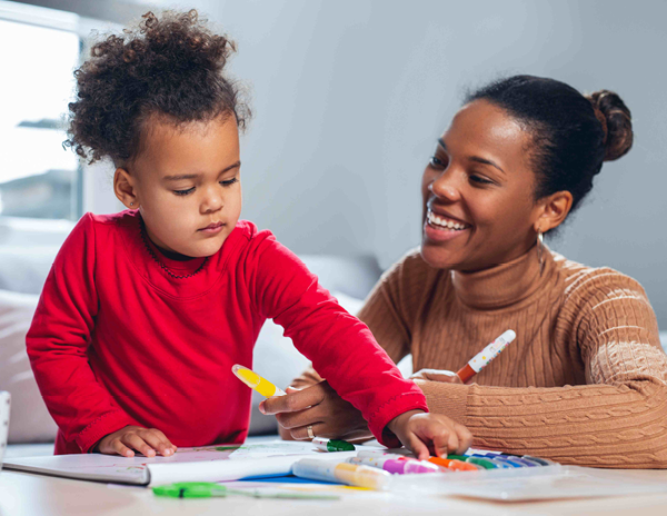 a woman and a child are sitting at a table playing with markers .