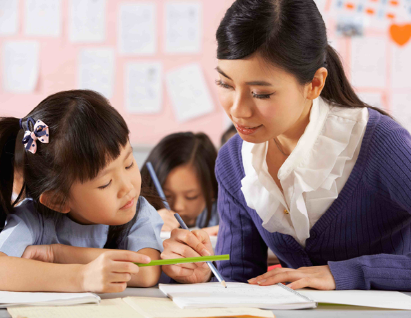 A teacher helping a little girl with her homework in a classroom