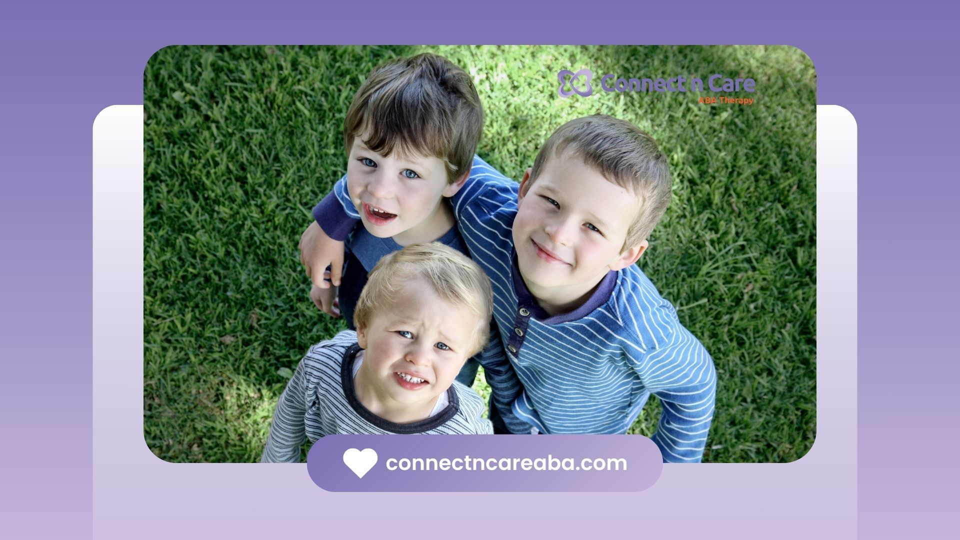 Three young boys are standing in the grass looking up at the camera.