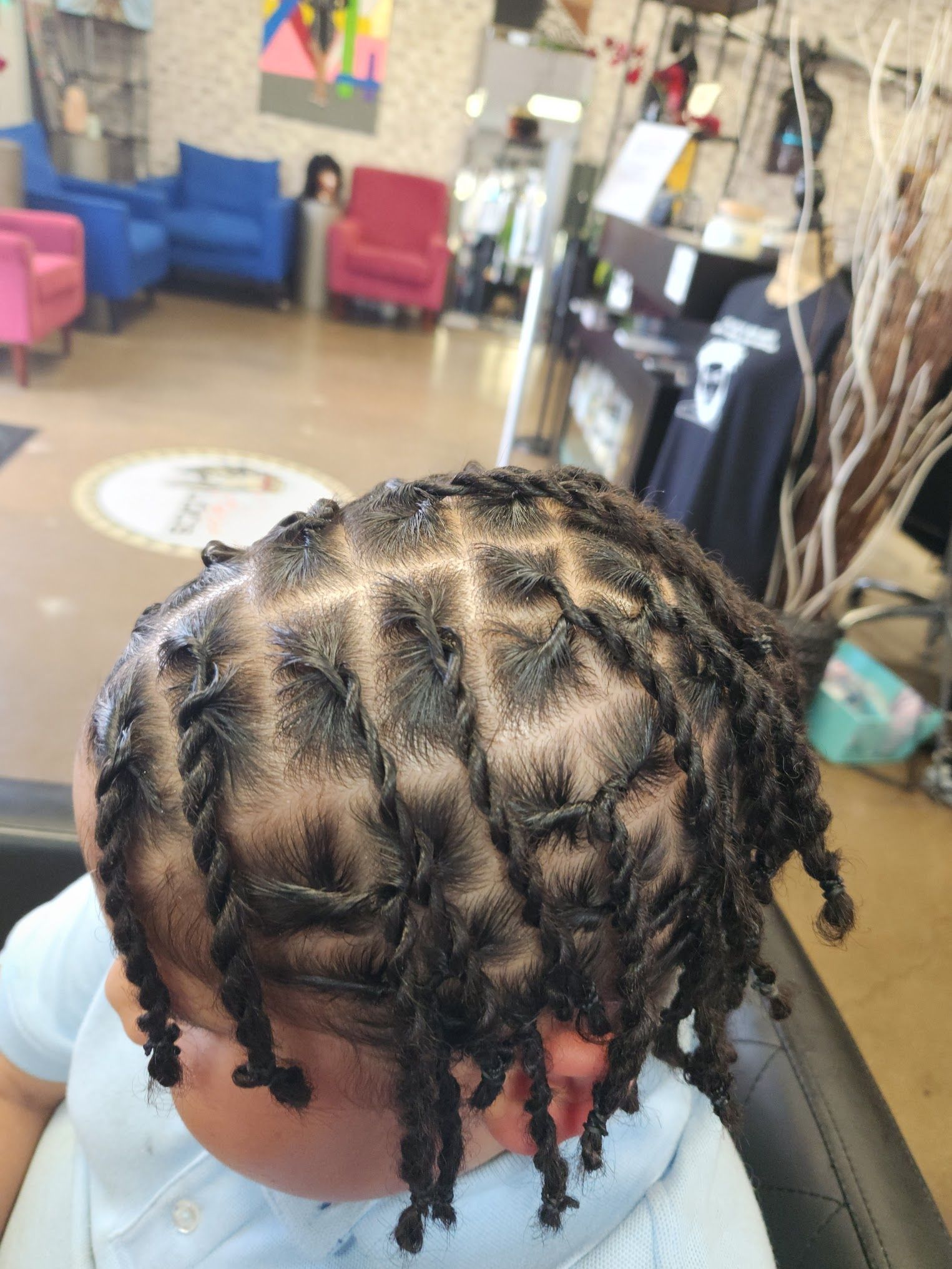 A baby with dreadlocks is sitting in a chair in a salon.