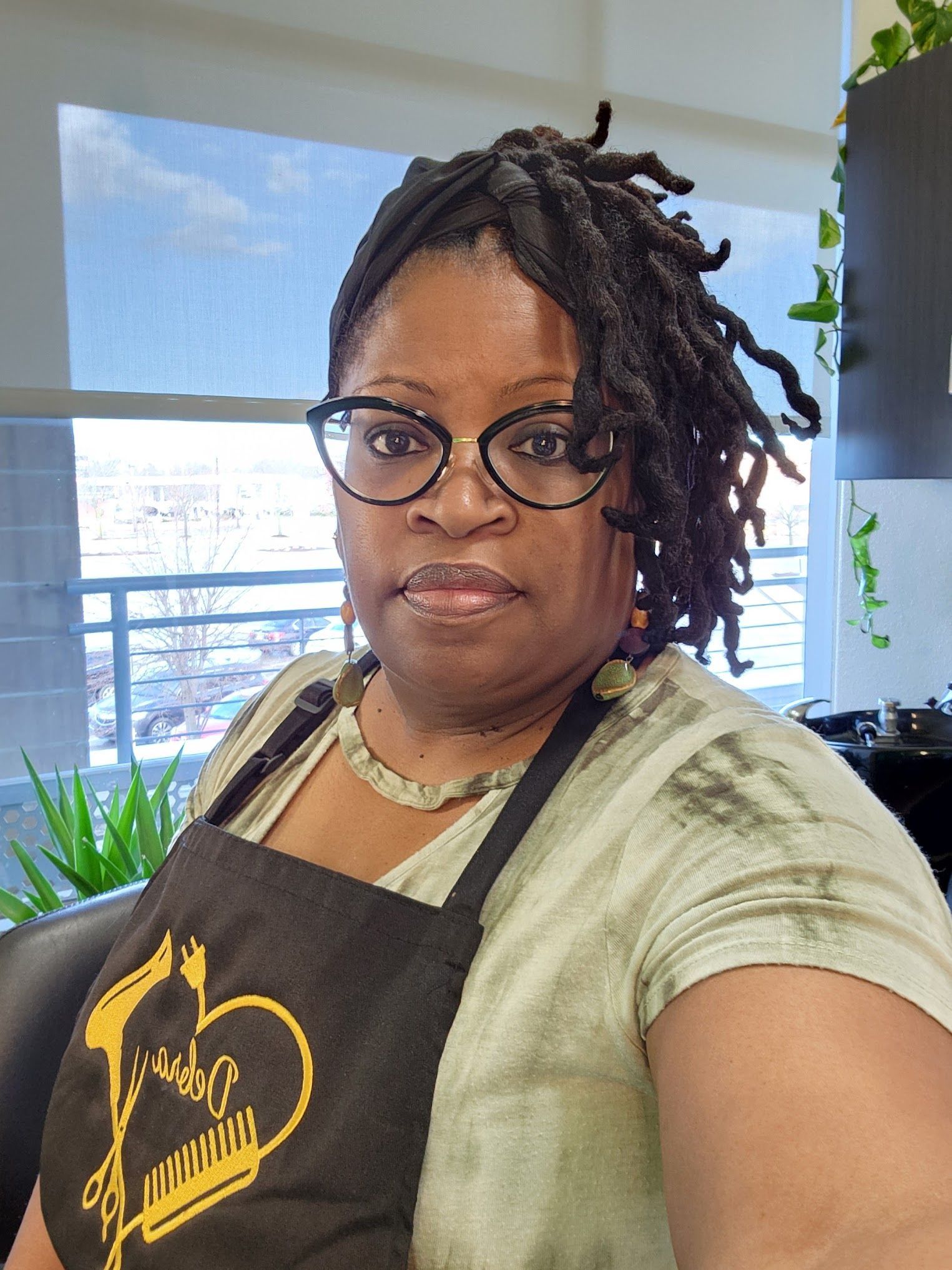 A woman with dreadlocks is wearing glasses and an apron.