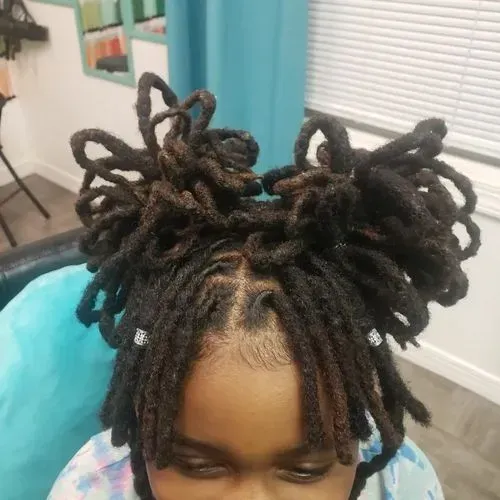 A young girl with dreadlocks is wearing a mask and sitting in a chair.