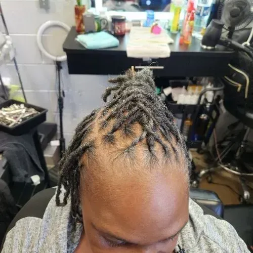 A man with dreadlocks is sitting in a chair in a salon.