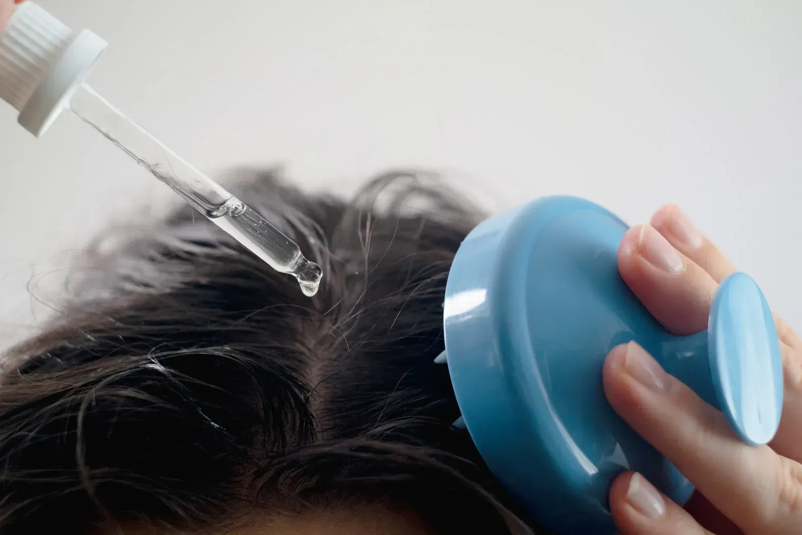 A person is applying a dropper to their hair.