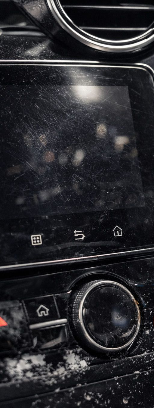 Close-up of a car's infotainment system. A black screen displays icons, a dial and a home button. Dust and snow are visible.