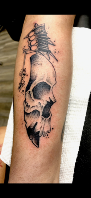 A person has a tattoo of a skull holding a dagger.