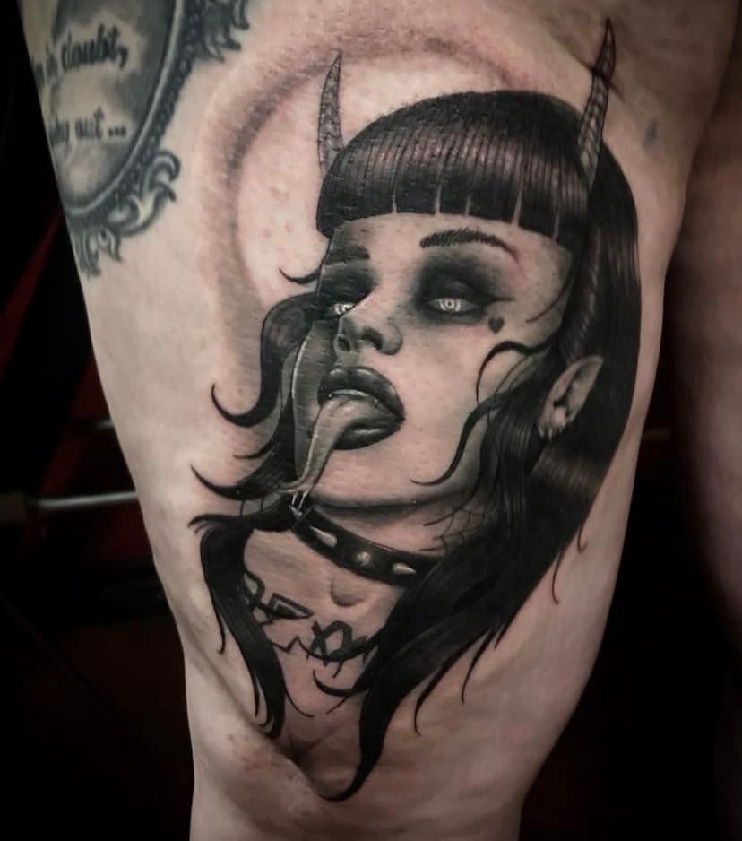 A black and white tattoo of a woman with horns sticking out her tongue
