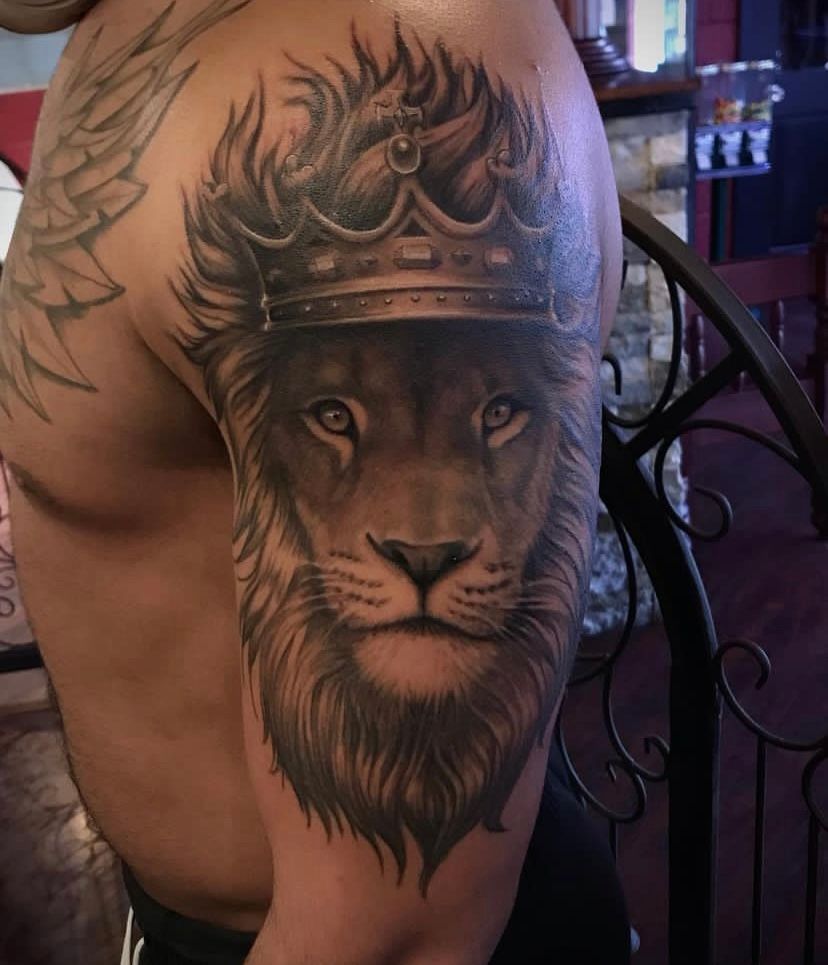 A man has a tattoo of a lion wearing a crown on his arm