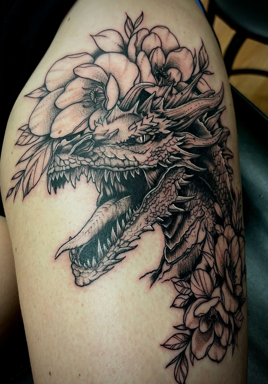 A black and white tattoo of a dragon surrounded by flowers