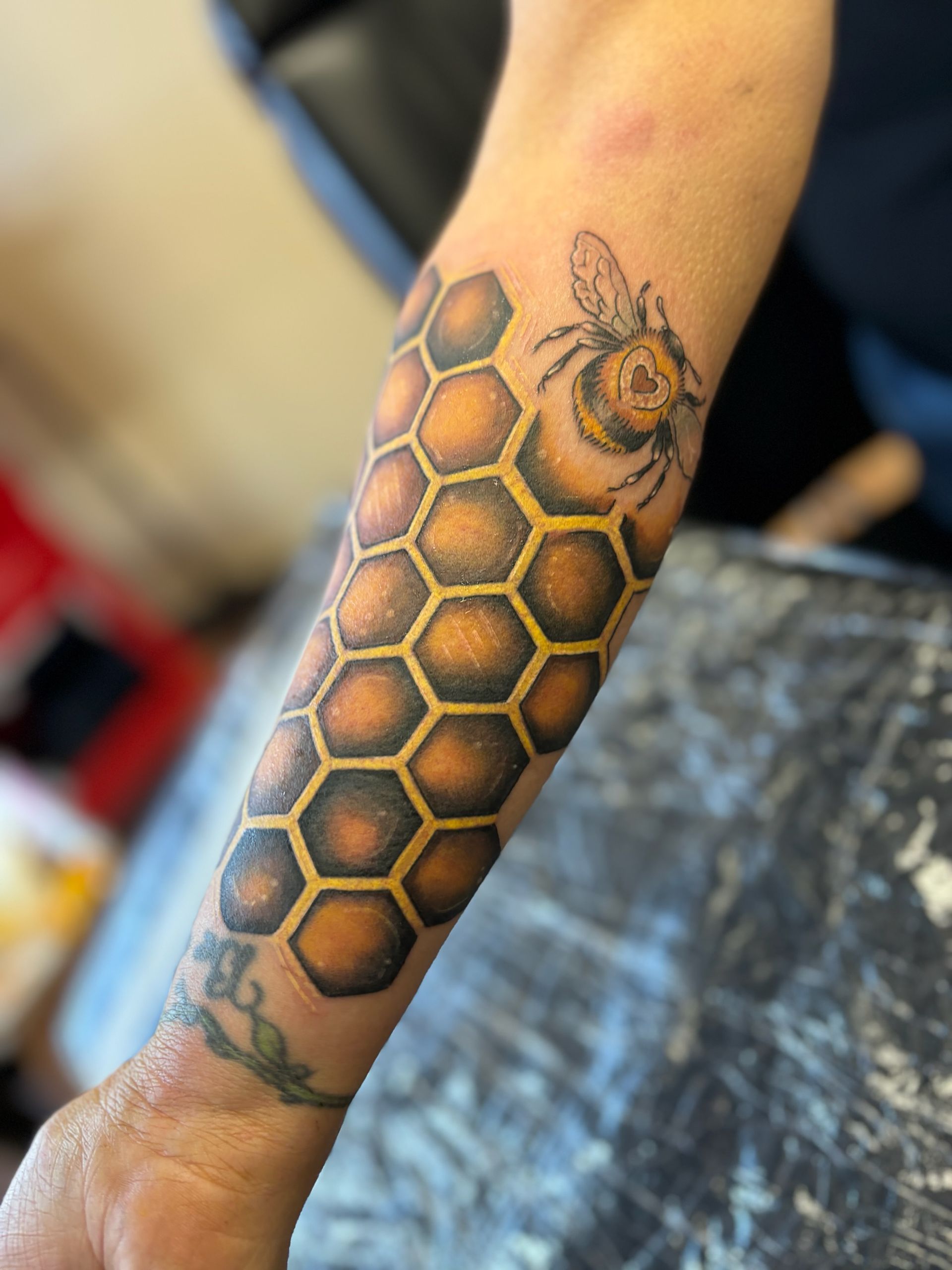 A person has a tattoo of a bee on a honeycomb on their arm.
