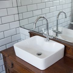 A general view of a modern bathroom square sink with tall chrome mixer tap sitting on an wooden dresser in front of a mirror