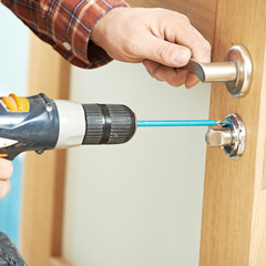 carpenter at lock installation with electric drill into interior wood door