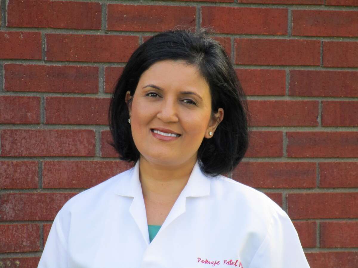 Woman with dark hair wearing a white lab coat smiles in front of a brick wall.