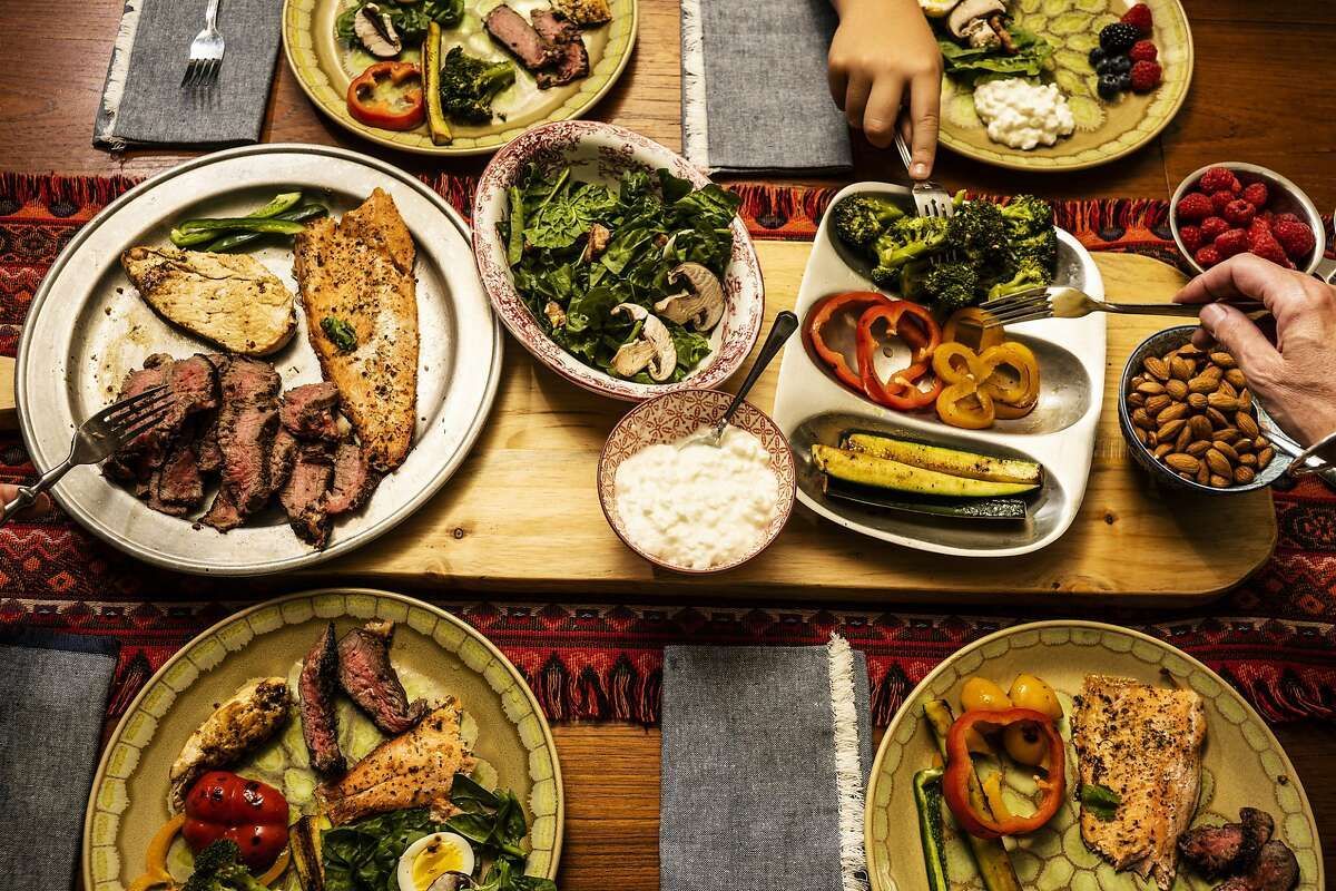 Overhead shot of a family meal featuring a variety of dishes: meats, vegetables, and sides, on a wooden table.