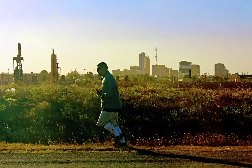 Man running on a path with city skyline in the background. Setting sun casts a warm glow.