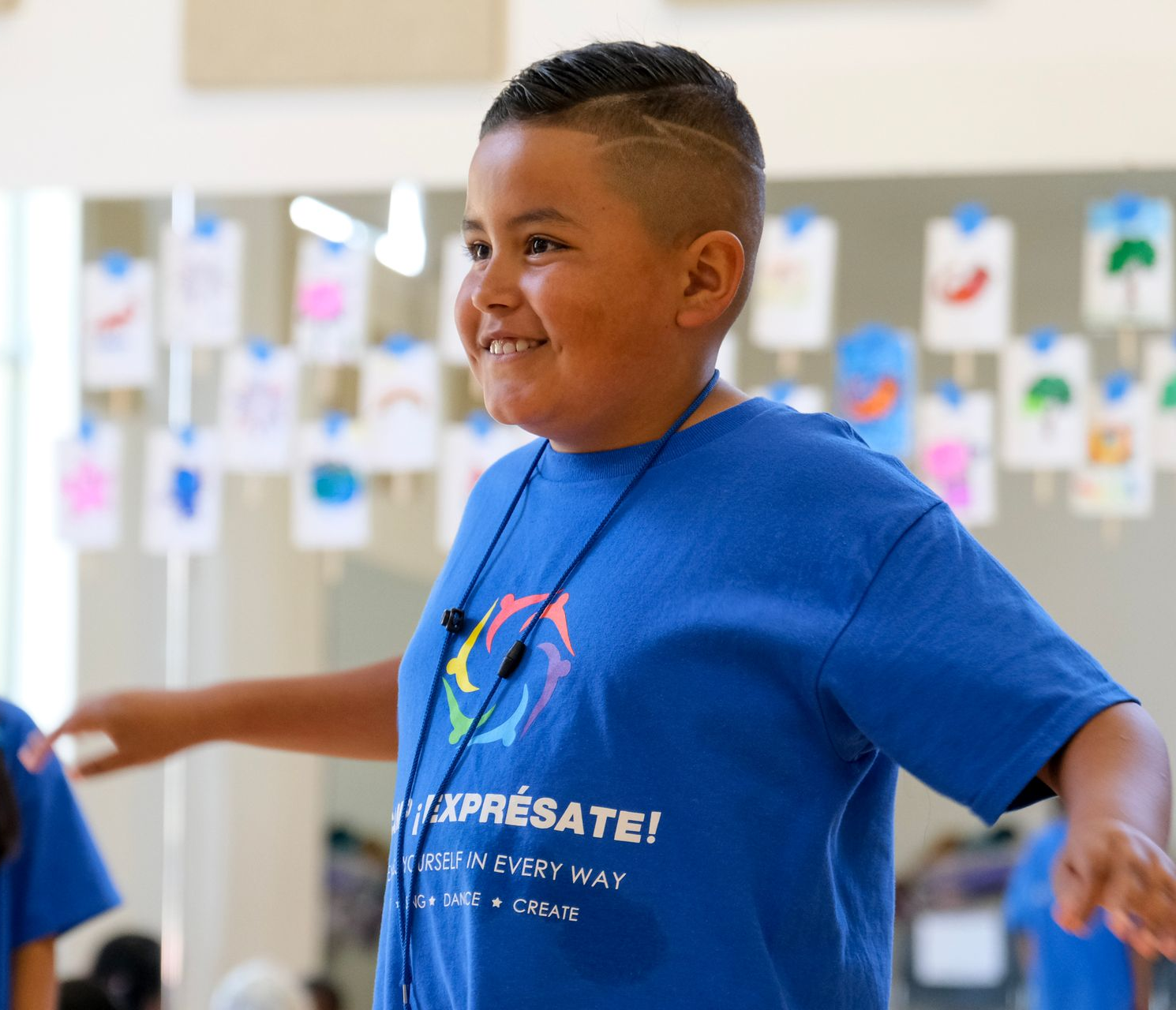 Boy in blue shirt smiling with arms outstretched, in a dance studio with colorful decorations.