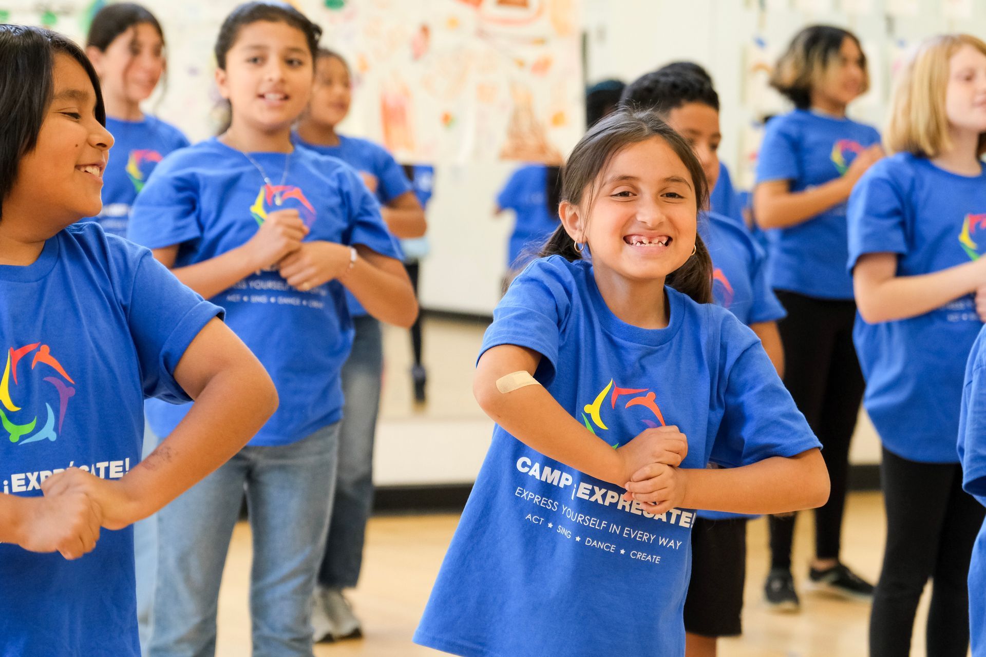Children in blue shirts dancing, smiling in a brightly lit studio.