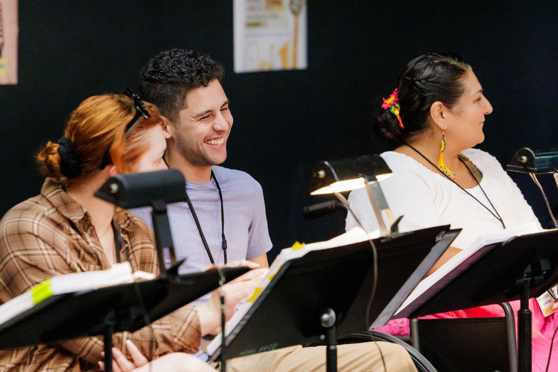 Three people smiling, sitting at music stands in a studio setting.