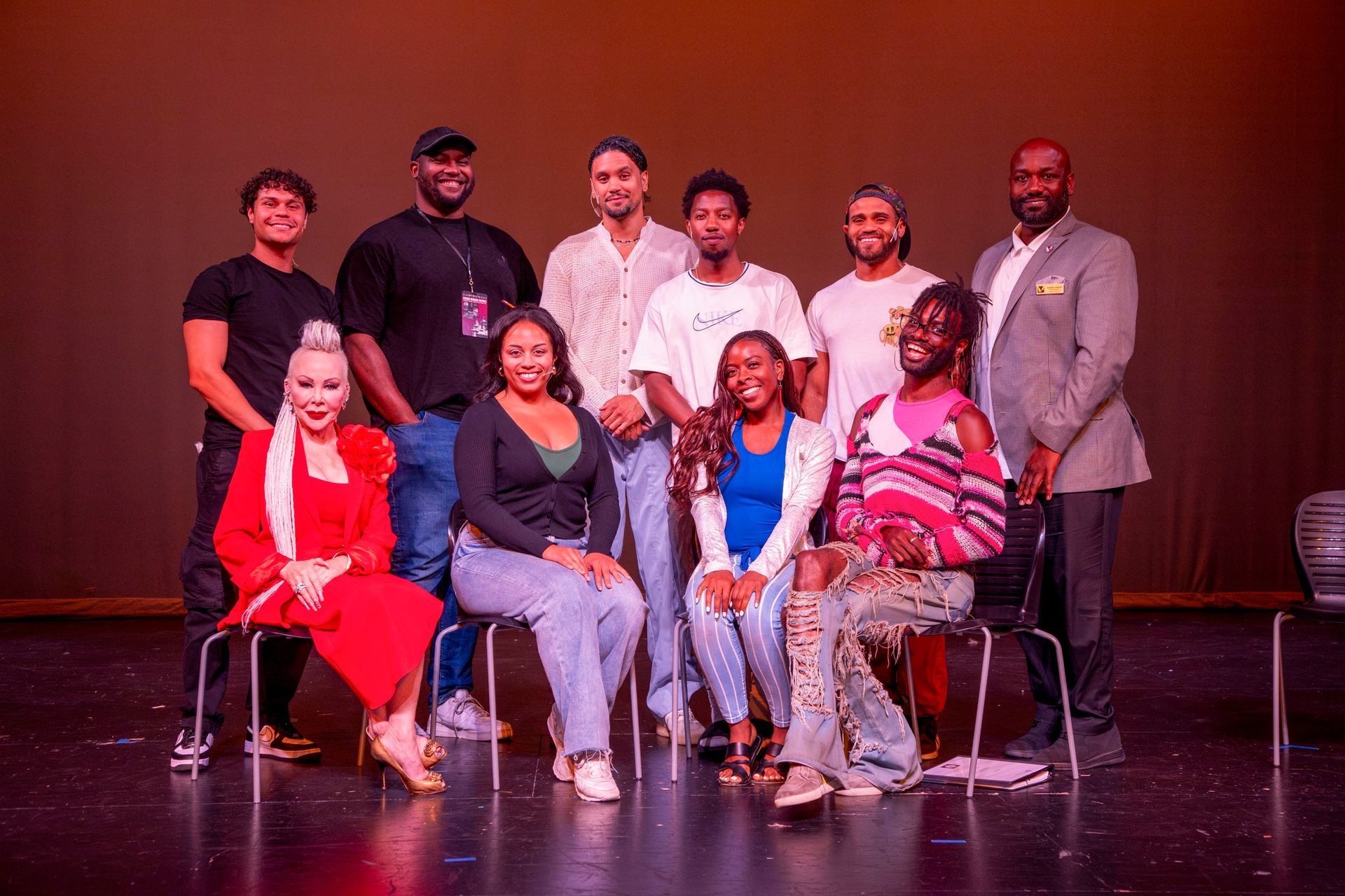 Group of people posing on a stage, some standing and some seated in chairs.