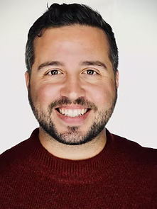 Man with short dark hair and a beard smiling, wearing a burgundy sweater.