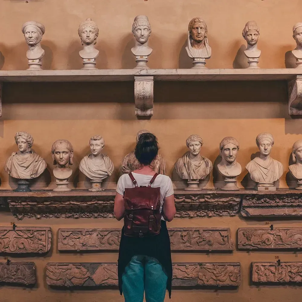Woman looking at classical busts in a museum; brown and cream decor.
