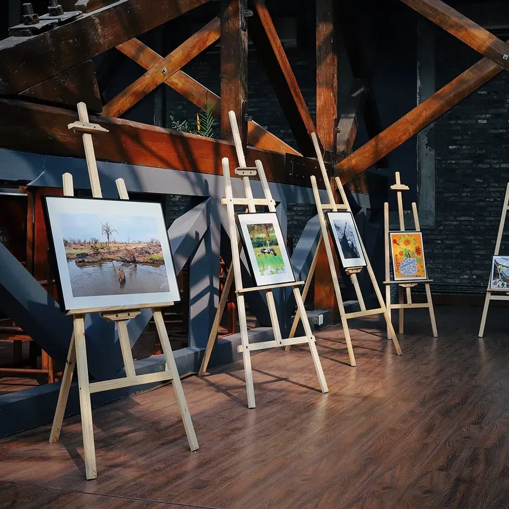 Art displayed on wooden easels in a room with a wooden beam ceiling.