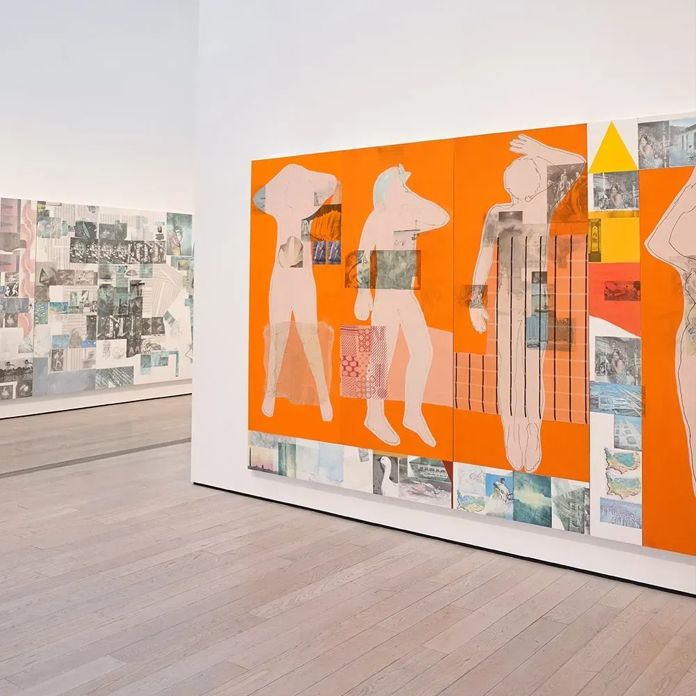 Modern art gallery with orange wall art and figures. Light wood floors, white walls.