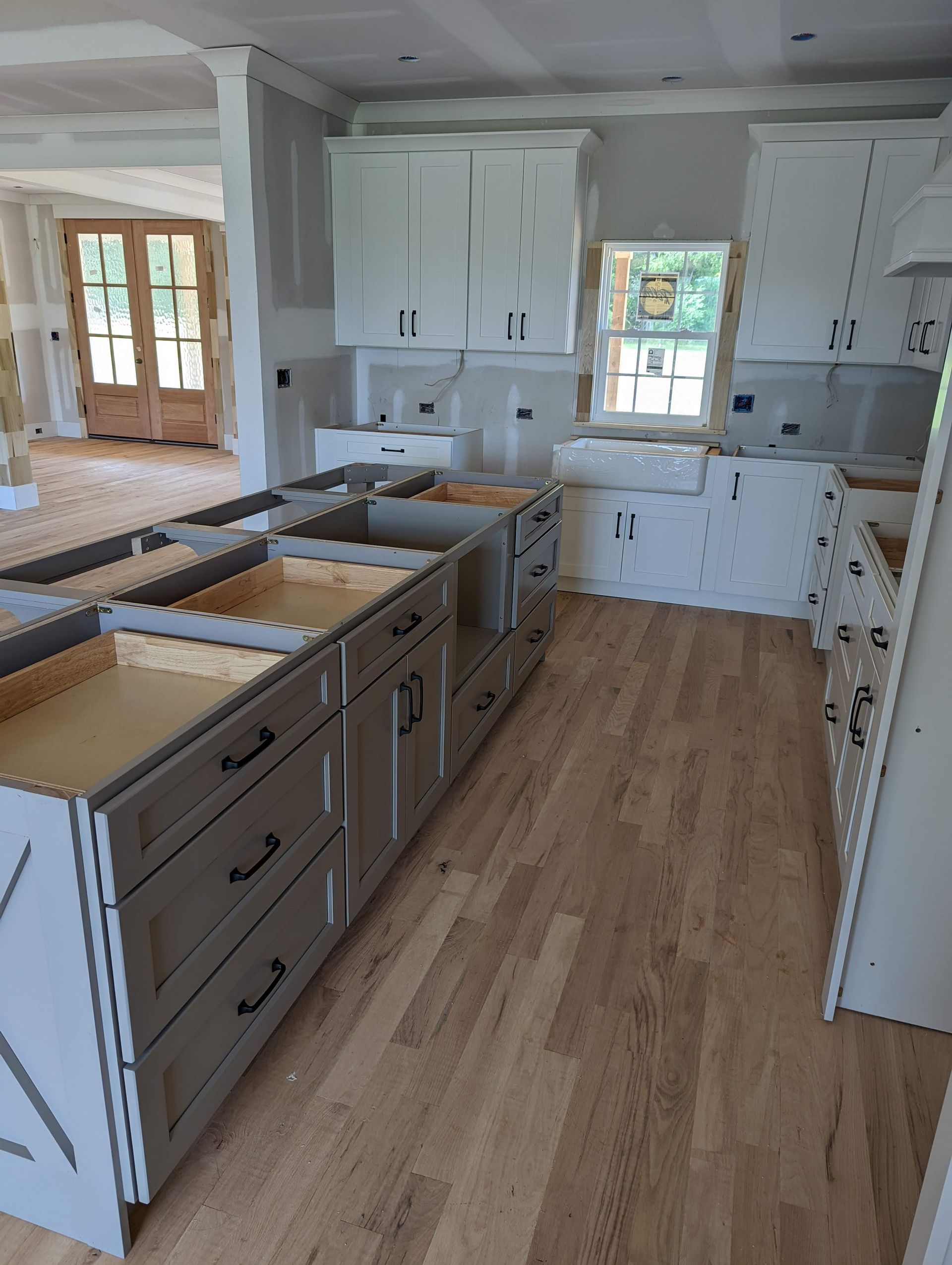 Kitchen under construction with light wood floors and gray cabinets. Upper cabinets are white.