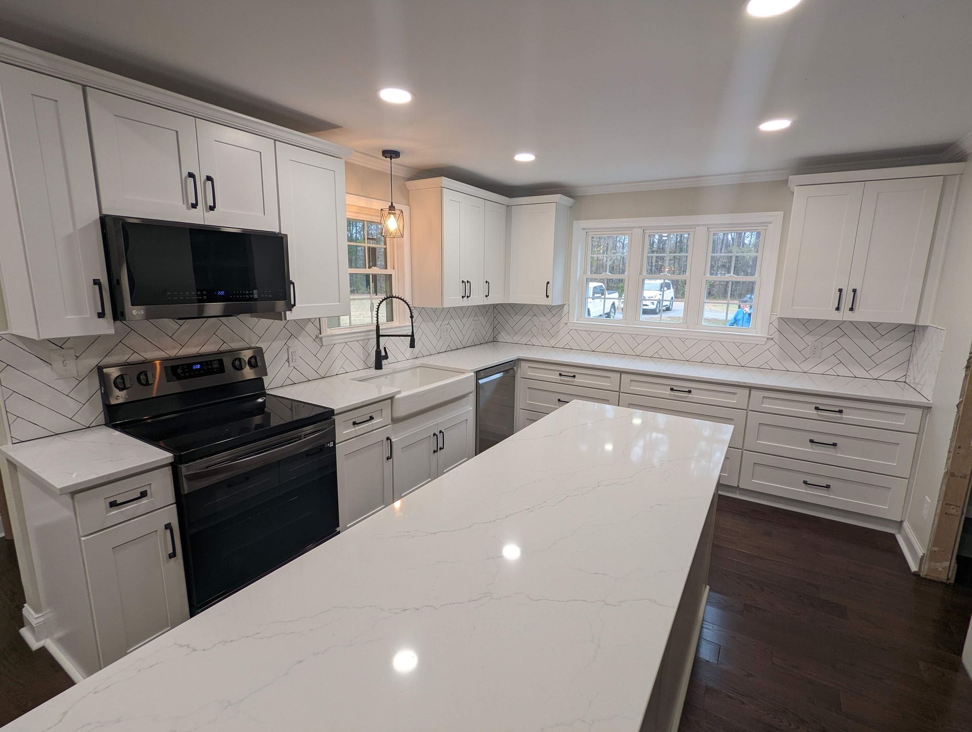 A bright, modern kitchen with white cabinets, countertops, and a large island. Features a black range, backsplash, and hardware.