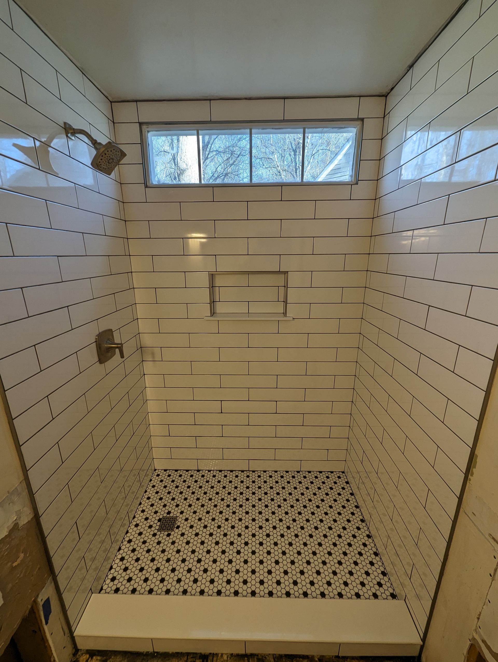A newly tiled shower with white subway tiles on the walls and black and white mosaic tile on the floor.