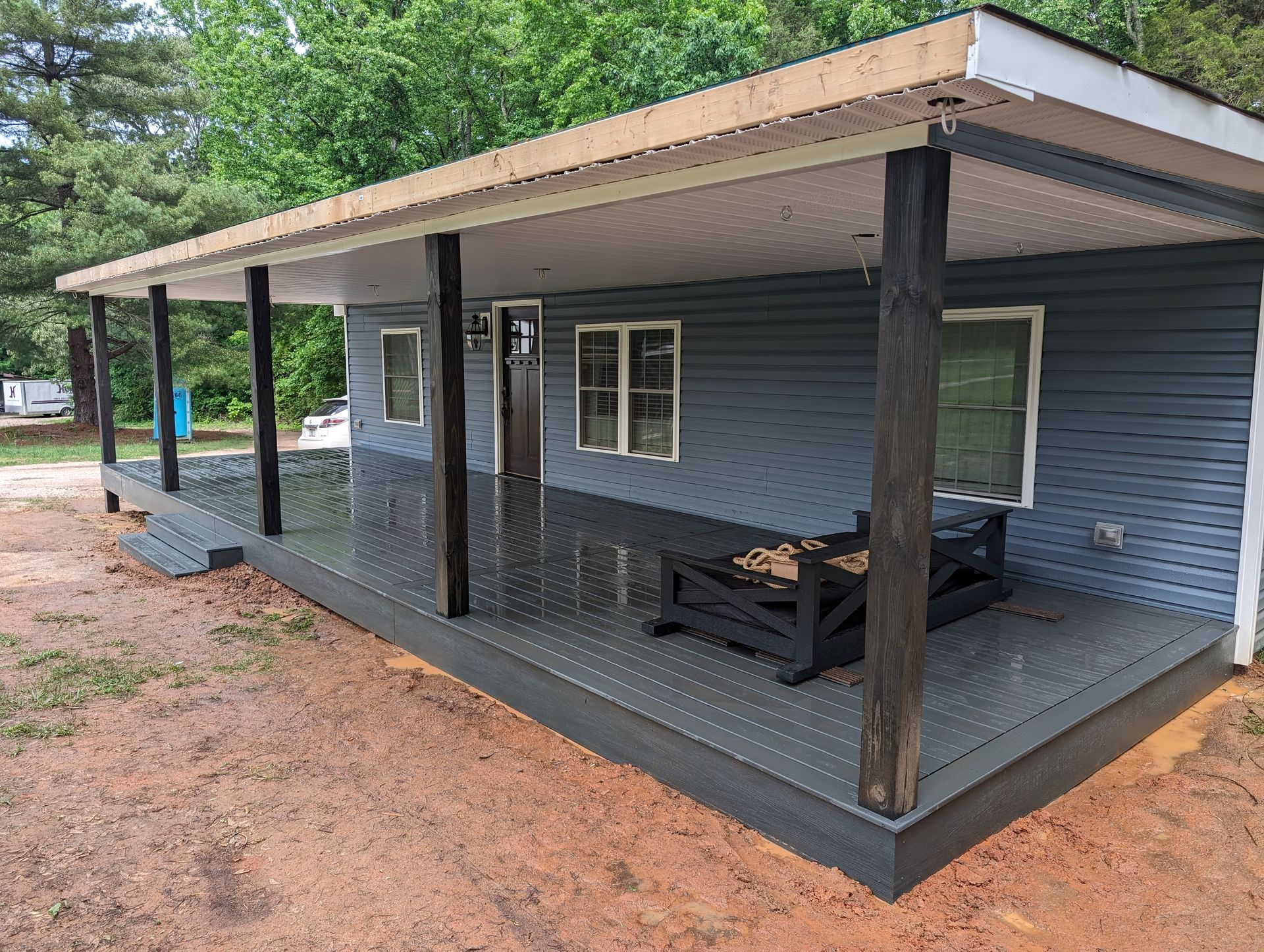 A small blue house with a covered porch and dark grey deck; set in a natural outdoor environment.