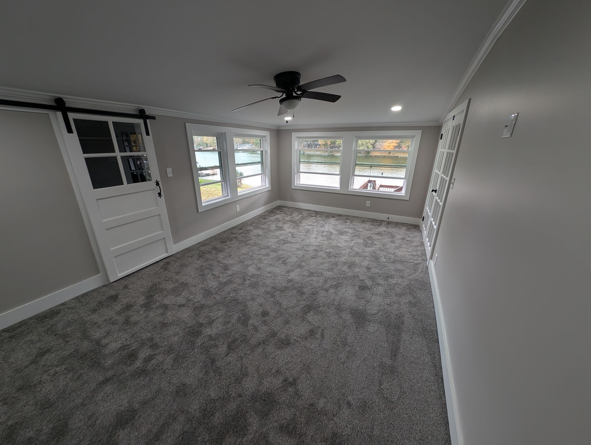 Empty room with gray carpet, windows, a sliding door, and a ceiling fan.