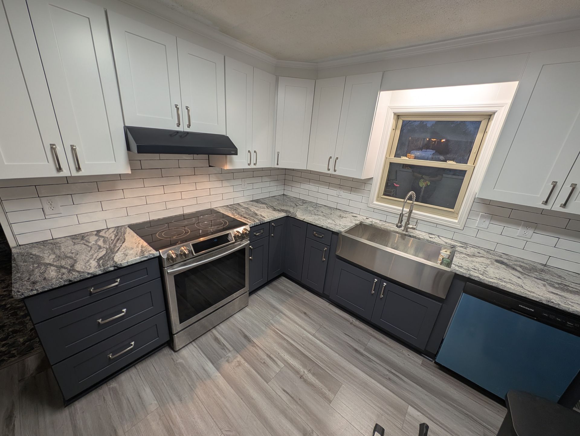 A modern kitchen with grey cabinets, stainless steel appliances, granite countertops, and a window over the sink.