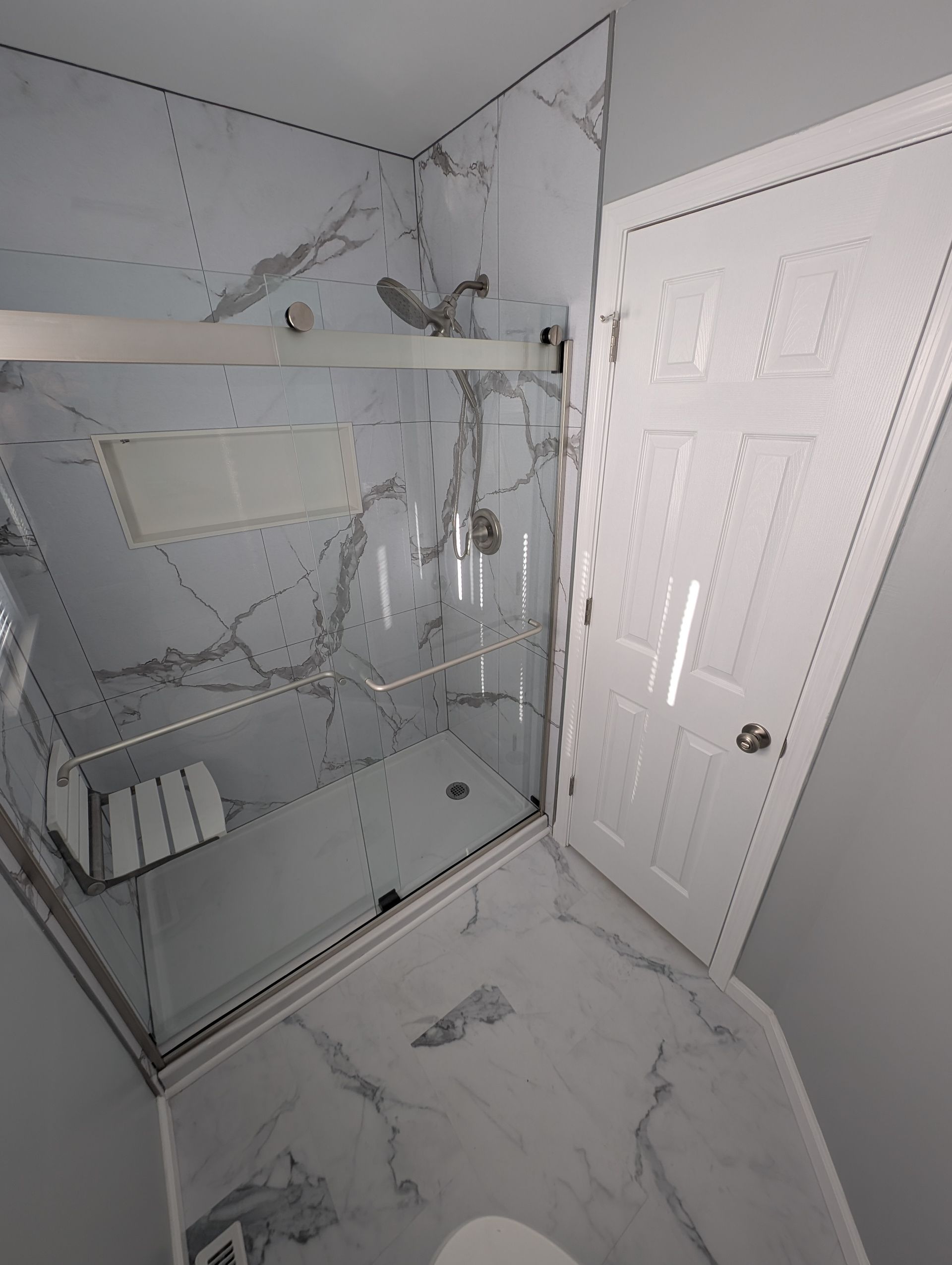 Modern bathroom with marble-look tiles, glass shower enclosure, and white door.