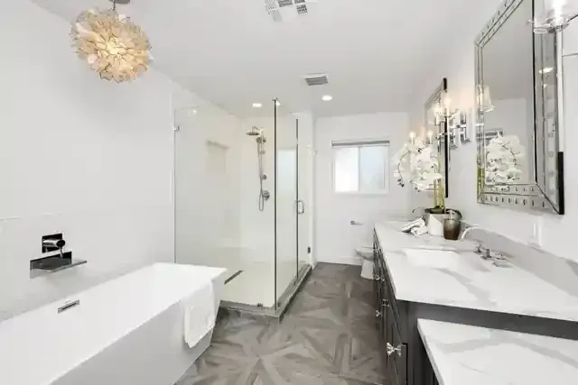 Modern white bathroom featuring a freestanding tub, glass-enclosed shower, dual-sink vanity, and patterned tile flooring.