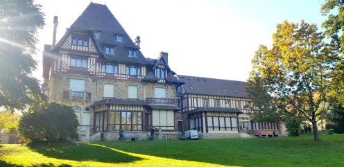 Grand bâtiment à plusieurs étages avec un toit pentu et une pelouse.