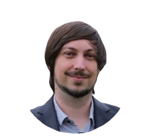 Homme aux cheveux bruns et à la barbe, souriant, portant une veste de costume et une chemise à col.