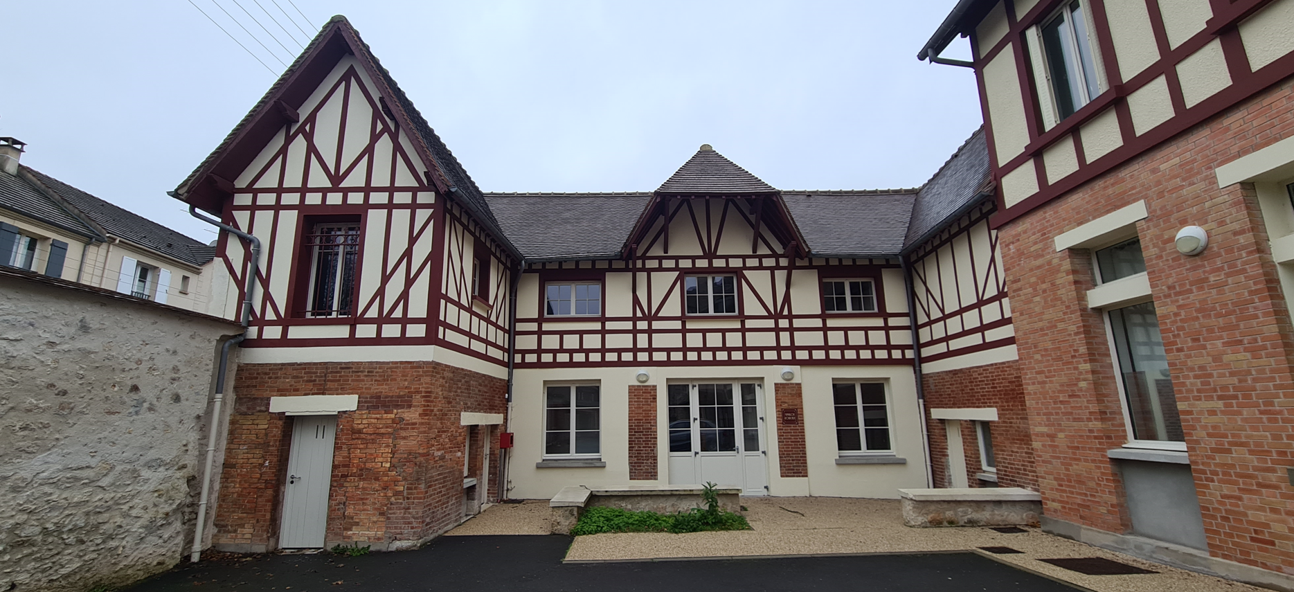 Un bâtiment de deux étages par temps nuageux. Façade en briques rouges de style Tudor blanc et brun.