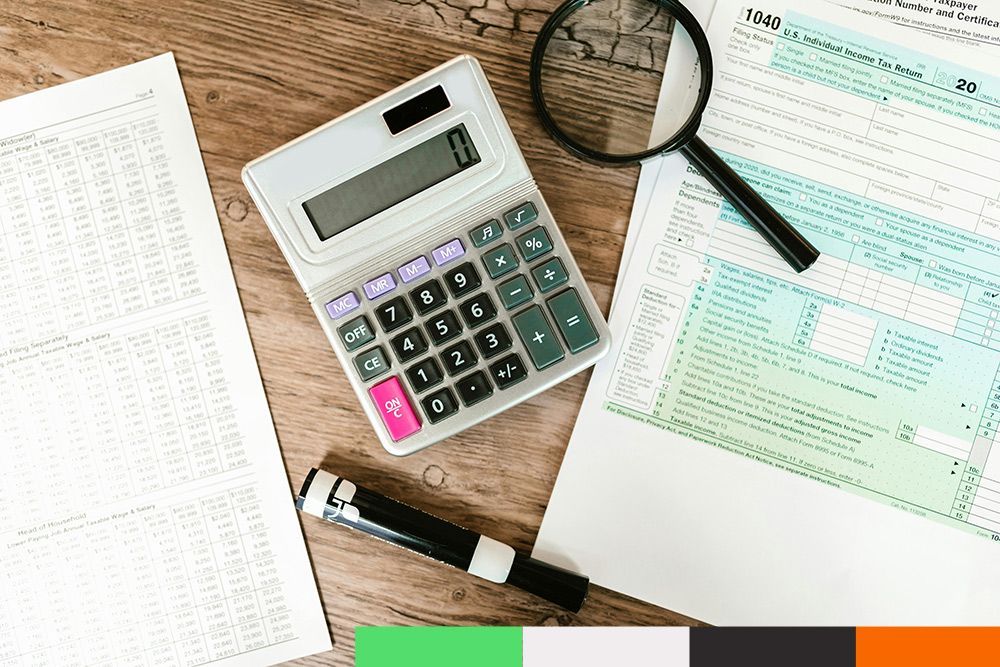 Une calculatrice, un stylo noir et une loupe posés sur des documents fiscaux fédéraux américains, eux-mêmes posés sur un bureau en bois.