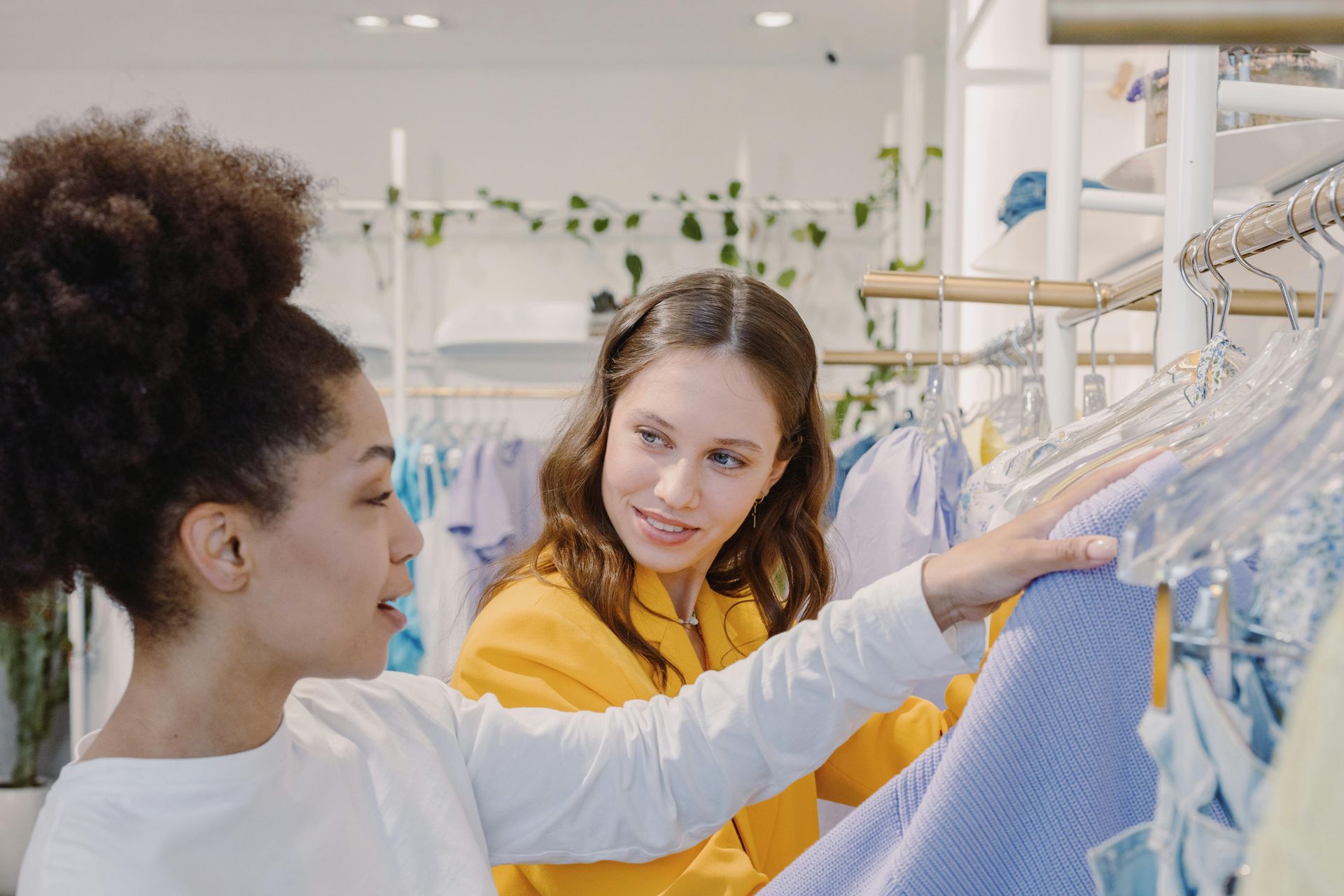 Deux personnes font leurs achats ensemble, regardant et touchant des vêtements sur un portant dans un magasin très éclairé.