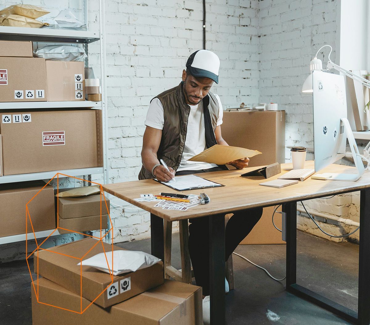 Dans un entrepôt, une personne portant une casquette et un gilet examine des documents à un bureau entouré de cartons d'expédition.