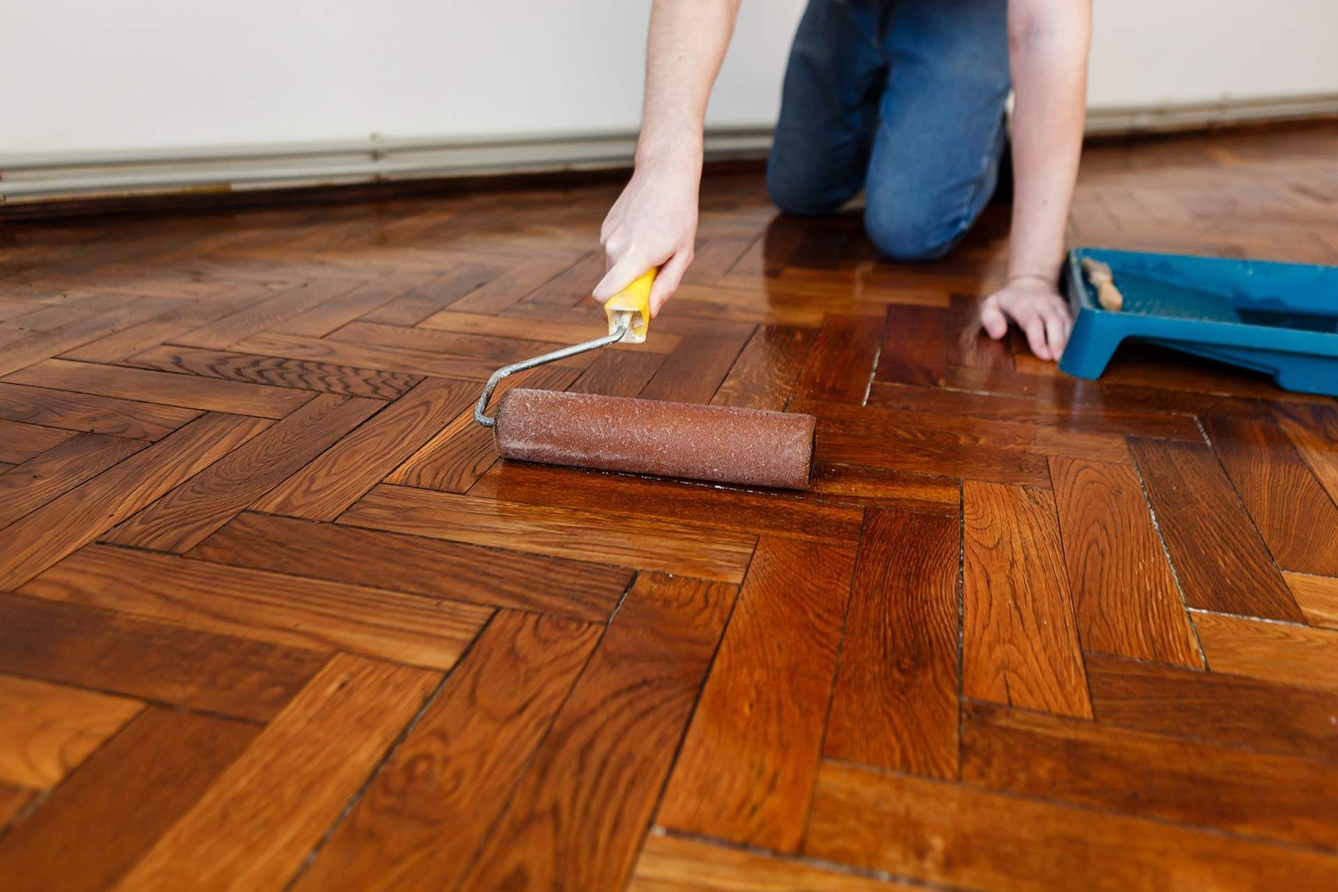 A person is painting a wooden floor with a roller.